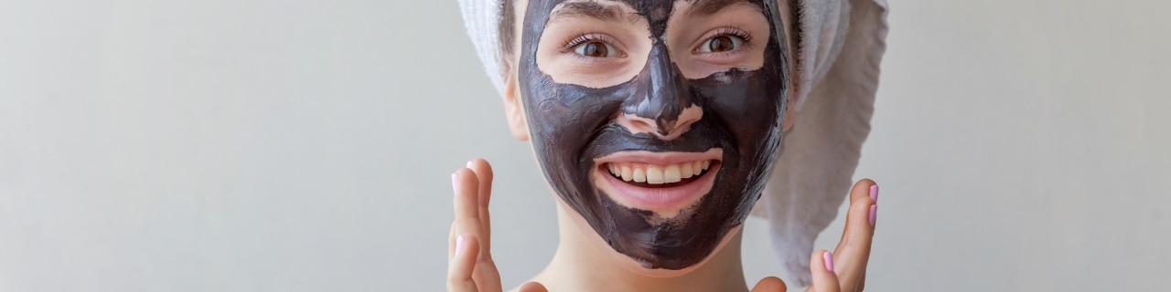 Mulher sorridente usando uma máscara de argila preta para hidratar o rosto