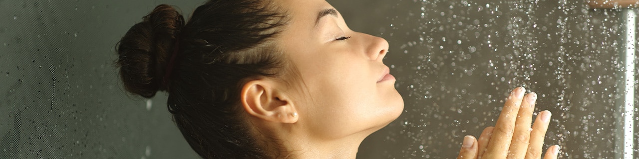 Mulher com expressão de tranquilidade de baixo do chuveiro, aproveitando os benefícios do banho gelado