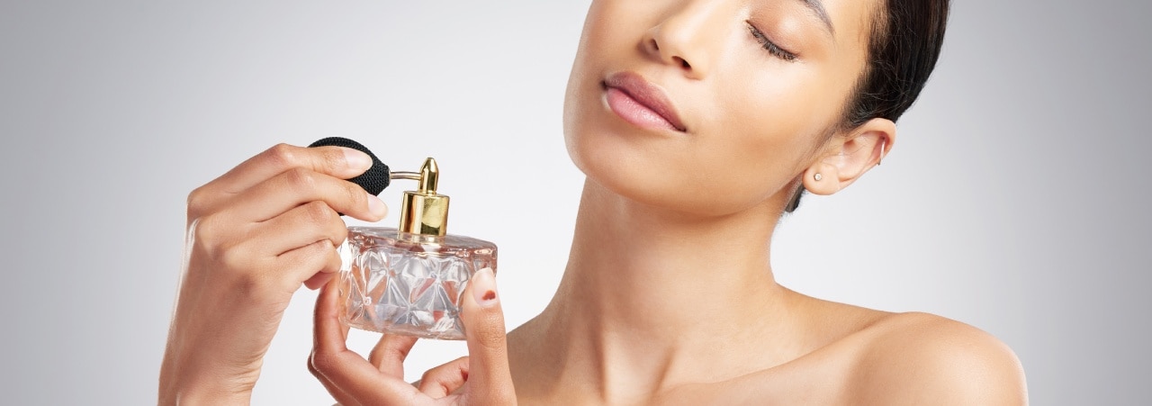 Mulher com olhos fechados aplicando perfume no pescoço, transmitindo a sensação de pele cheirosa e bem cuidada no dia a dia.