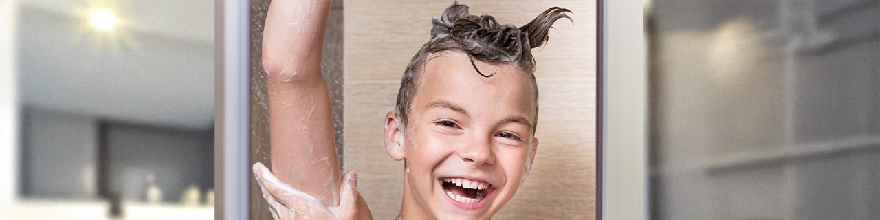 Menino sorridente lavando o cabelo com um shampoo infantil durante o banho
