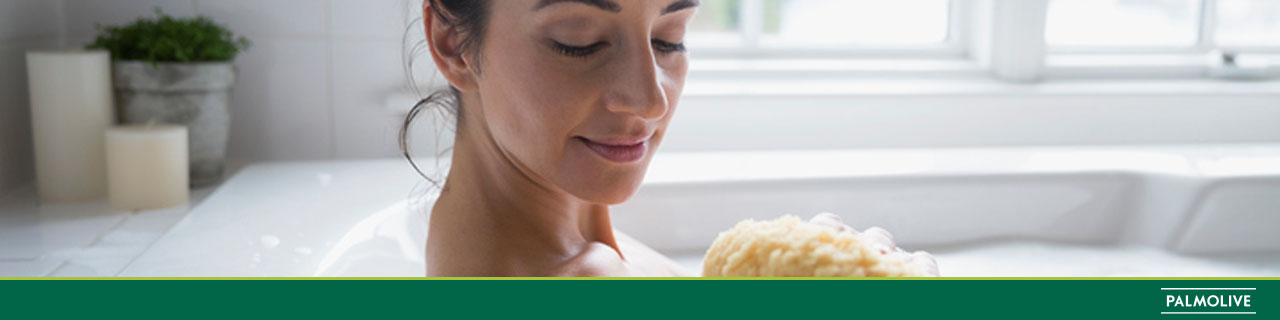 Mulher sentada na banheira tomando banho e passando no corpo o sabonete de carvão