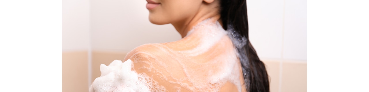 Mulher tomando banho com um sabonete em barra barato, mas que oferece hidratação e maciez para sua pele. 