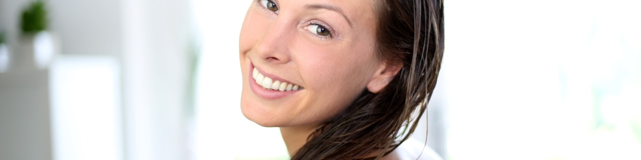 Mulher sorridente com cabelos úmidos após aplicar condicionador anticaspa no comprimento dos fios.