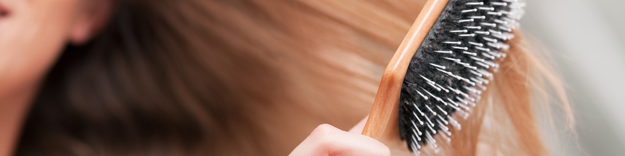 Uma mulher penteando o cabelo, observando atentamente a saúde dos fios para entender como saber se seu cabelo está danificado