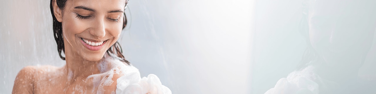 Mulher sorridente no chuveiro com o corpo coberto por espuma de um sabonete líquido barato e de qualidade