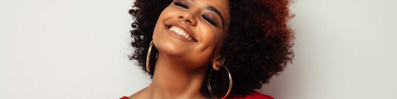 Mulher com cabelos cacheados, sorrindo de felicidade, pois seus fios estão hidratados e macios após o uso correto do shampoo e condicionador para cachos.  